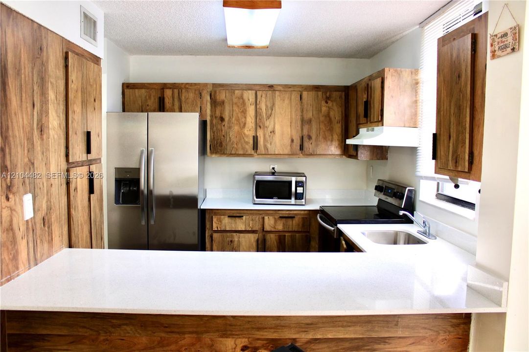 Kitchen featuringwhite solid-surface countertops, a stainless steel refrigerator, an integrated microwave, and an undermount sink