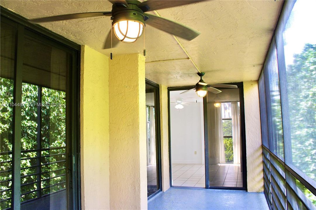 Screened-in balcony featuring dual ceiling fans with integrated globe lighting, textured ceiling, and metal-frame screen enclosure