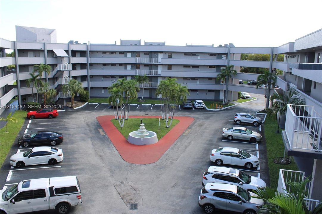 Multi-level exterior architecture featuring open-air walkways, a central courtyard with a decorative fountain, and lush palm landscaping