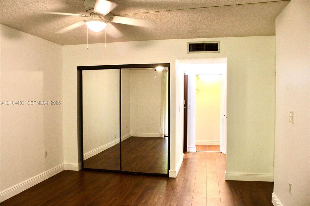 Wood-finish flooring, ceiling fan with integrated lighting, and mirrored sliding closet doors