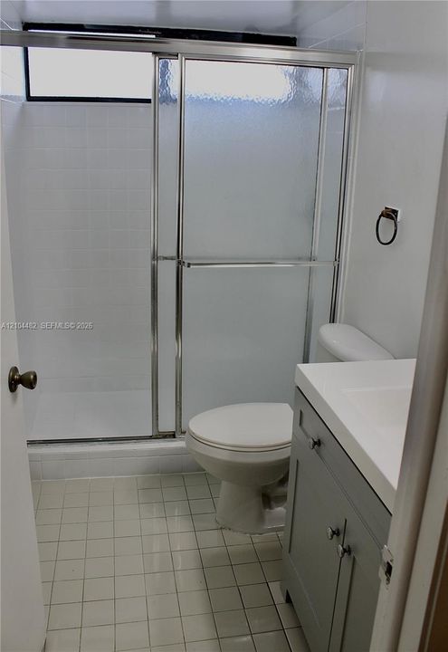 Bathroom featuring a gray vanity with an integrated sink, shower enclosure with sliding textured glass doors, tiled walls, and ceramic tile flooring