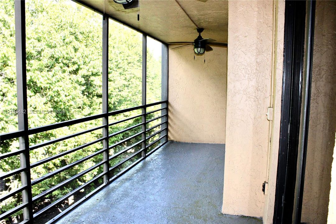 Screened-in balcony featuring a concrete floor, metal railings, and a ceiling-mounted light fixture with a fan