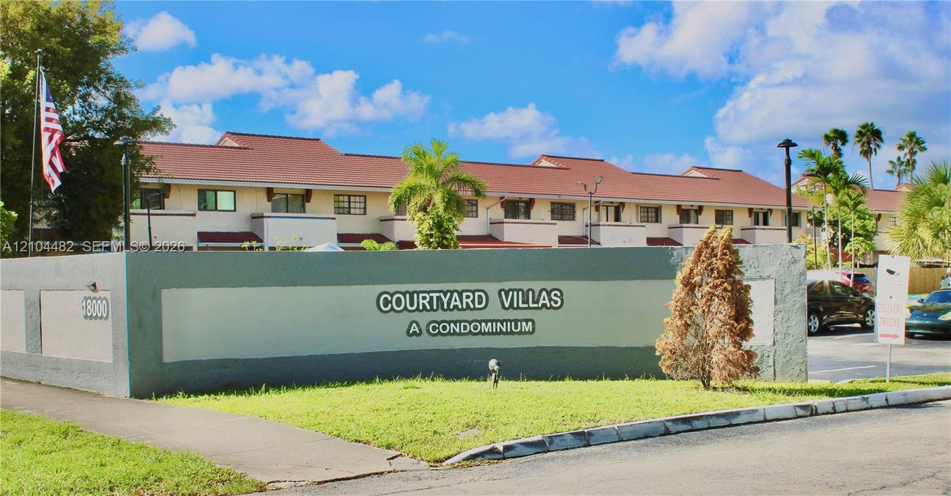 Multi-story condominium exterior featuring a tiled roof, stucco facade, and exterior lighting fixtures