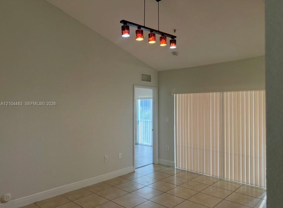 Vaulted ceiling with track lighting, tiled flooring, and vertical blinds