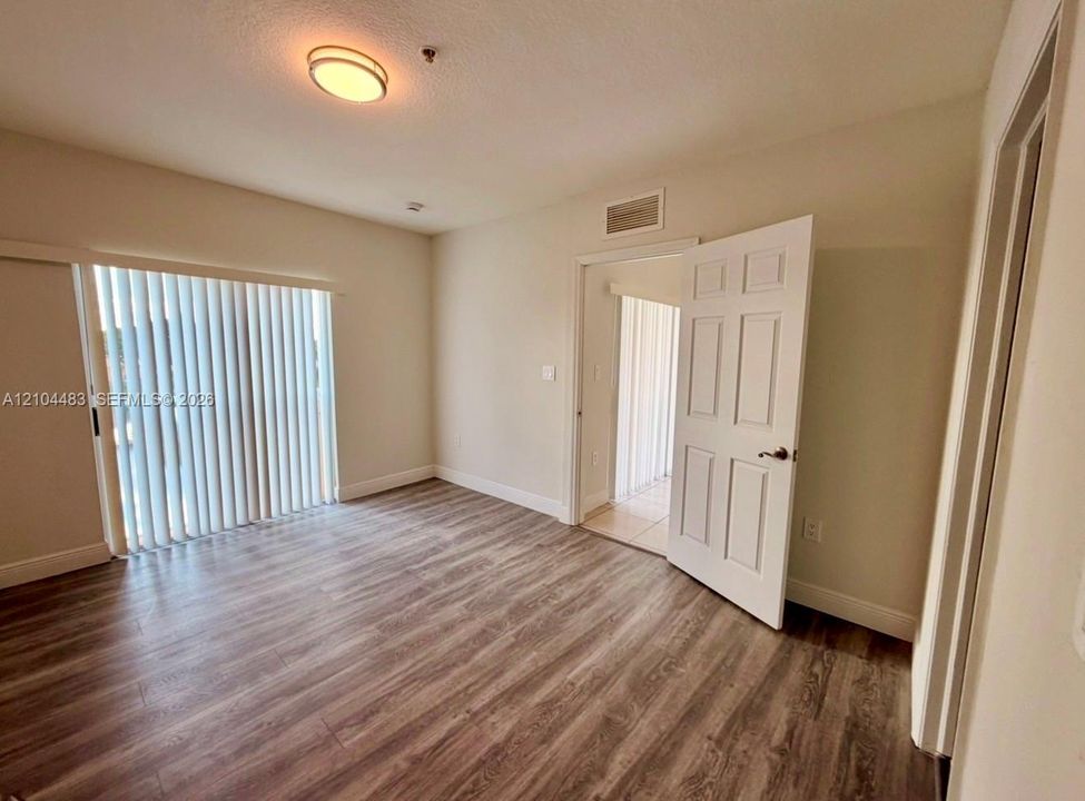 Wood-finish flooring throughout, sliding glass door with vertical blinds, recessed ceiling light, and paneled interior door