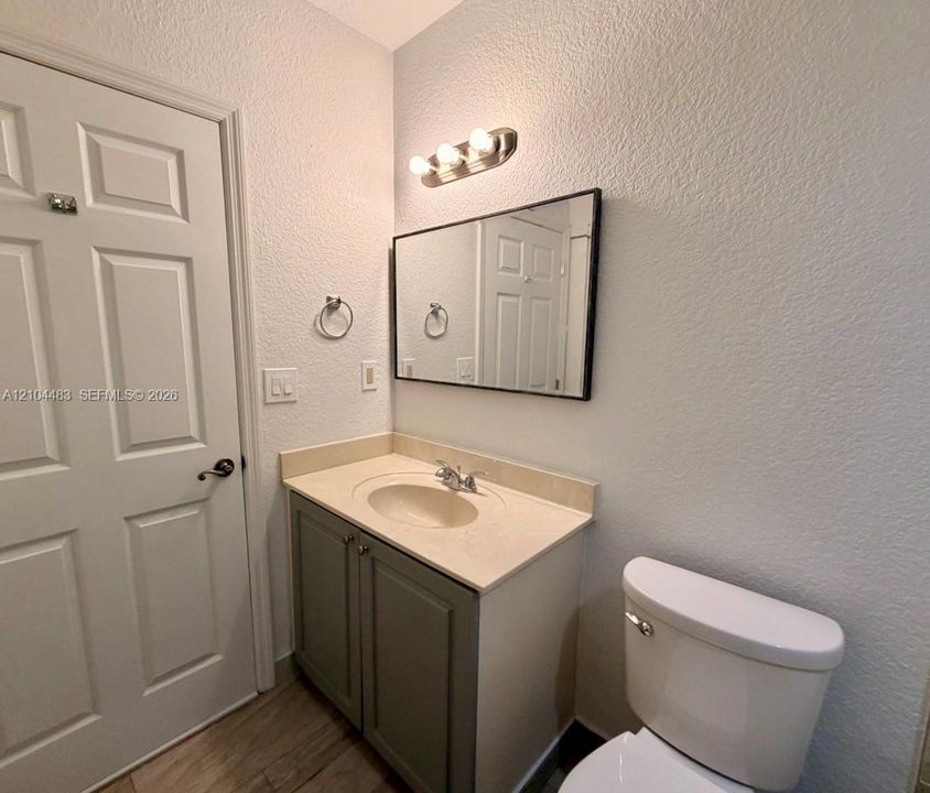 Bathroom featuring a single vanity with a light-toned countertop, an integrated sink, a vanity cabinet with double doors, a rectangular mirror, and a wall-mounted light fixture