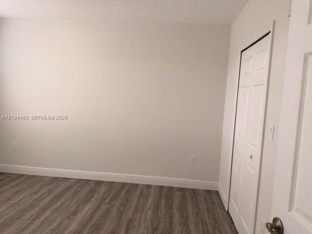 Wood-finish flooring with white trim, light-colored textured walls, and a bi-fold closet door