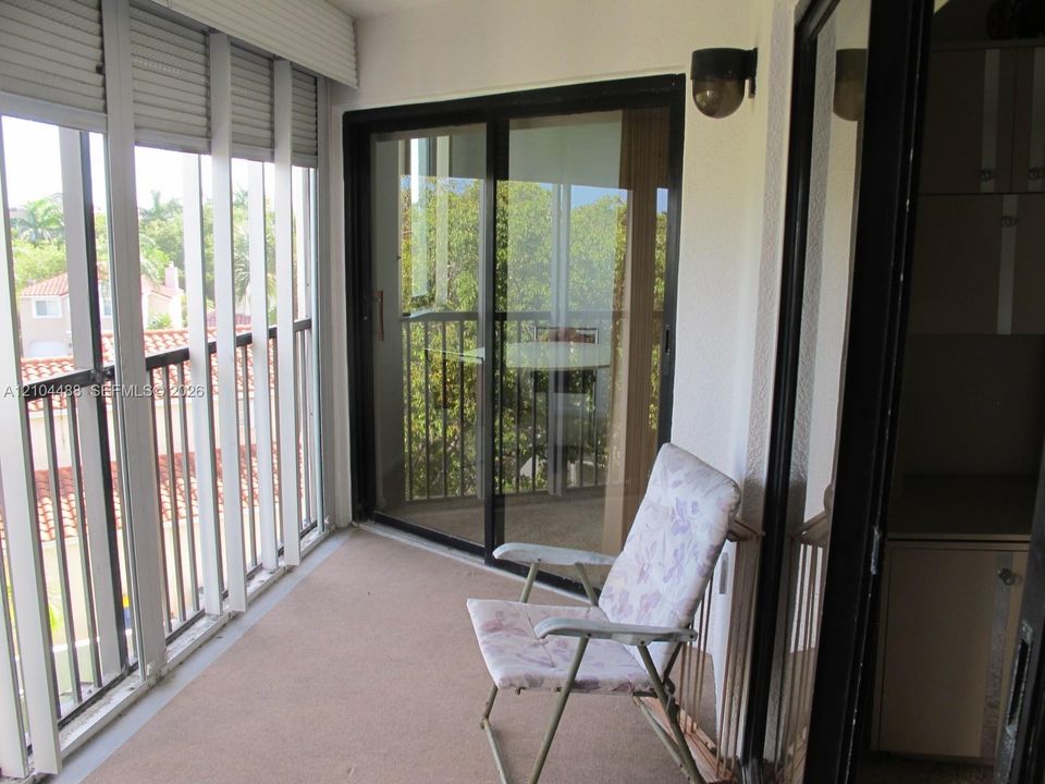 Screened balcony with sliding glass doors, white exterior shutters, and a built-in wall sconce