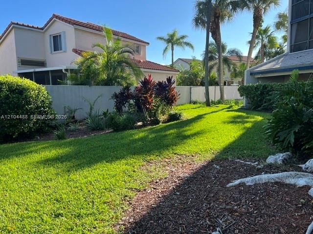 Backyard featuring a manicured lawn, established landscaping, mature palm trees, and a privacy wall