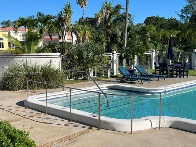 Swimming pool with a metal safety rail, concrete decking, and perimeter fencing, surrounded by mature palm trees and landscaping