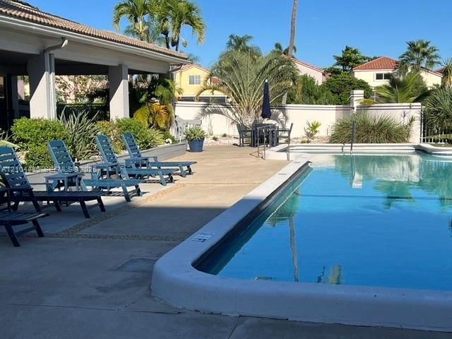 Rectangular swimming pool with a concrete surround, covered patio, privacy wall, and mature landscaping