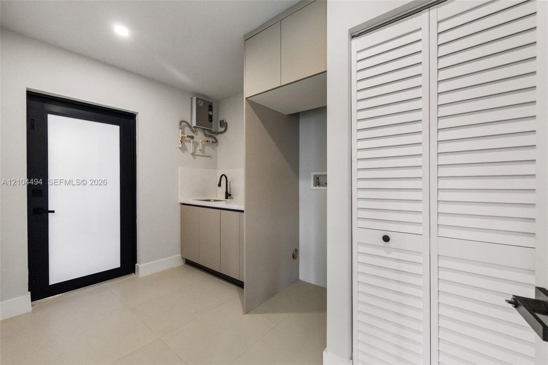 Utility space featuring custom cabinetry, integrated sink with matte black fixture, louvered closet doors, and black-framed glass-panel door