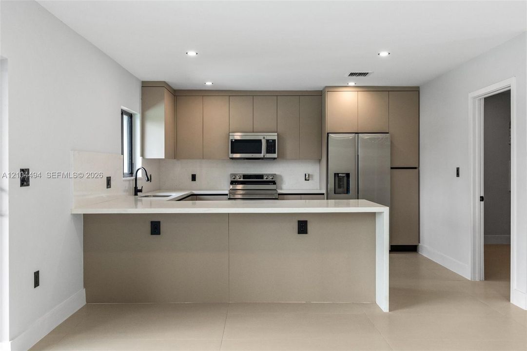 Kitchen featuring flat-panel cabinetry, quartz countertops with a waterfall edge, stainless steel appliances, recessed lighting, and large-format tile flooring