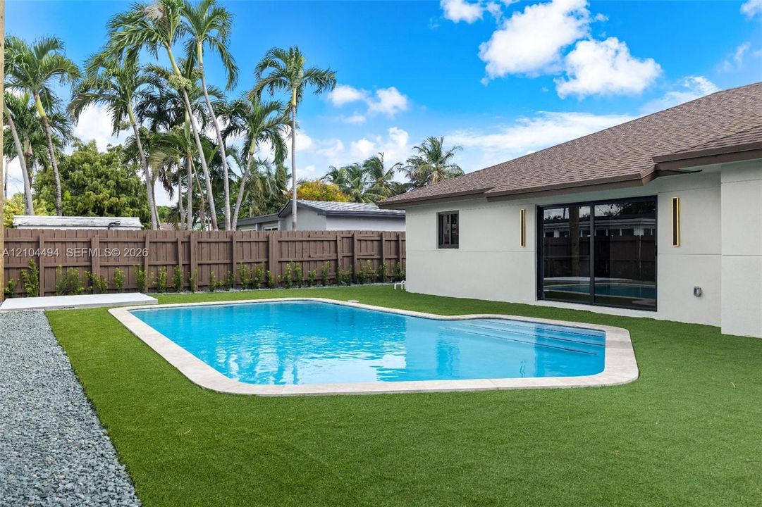 In-ground swimming pool with integrated stairs, low-maintenance artificial turf, privacy fencing, and exterior wall-mounted lighting