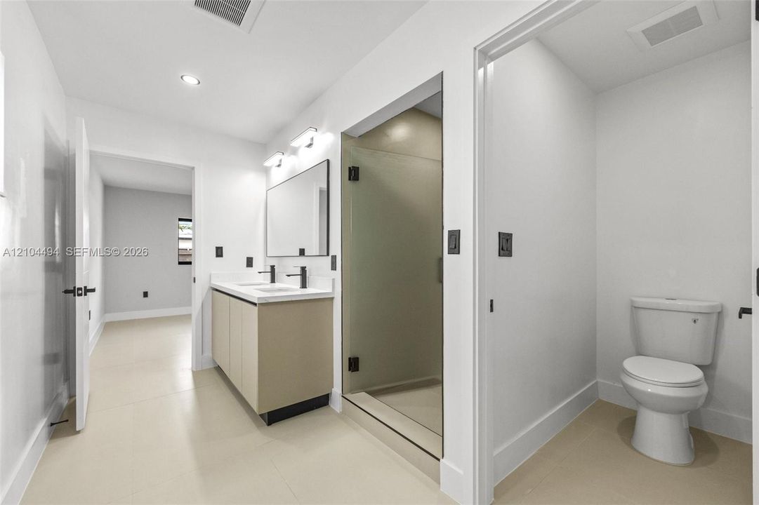 Bathroom featuring a floating vanity with a light-tone finish, rectangular dual-basin countertop, glass-enclosed shower with matte black hardware, and tile flooring