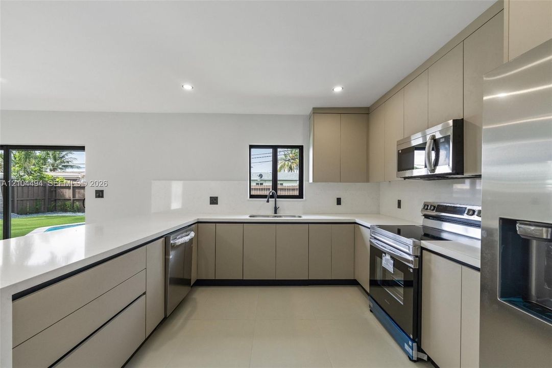Kitchen featuring flat-panel cabinetry, quartz countertops, solid-surface backsplash, stainless steel appliances, and recessed lighting