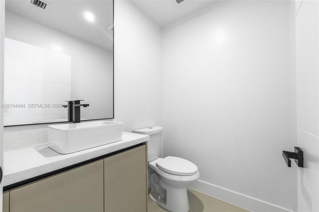 Vanity featuring a rectangular vessel sink, quartz countertop, matte black faucet, and frameless mirror, paired with a two-piece toilet and matching matte black hardware