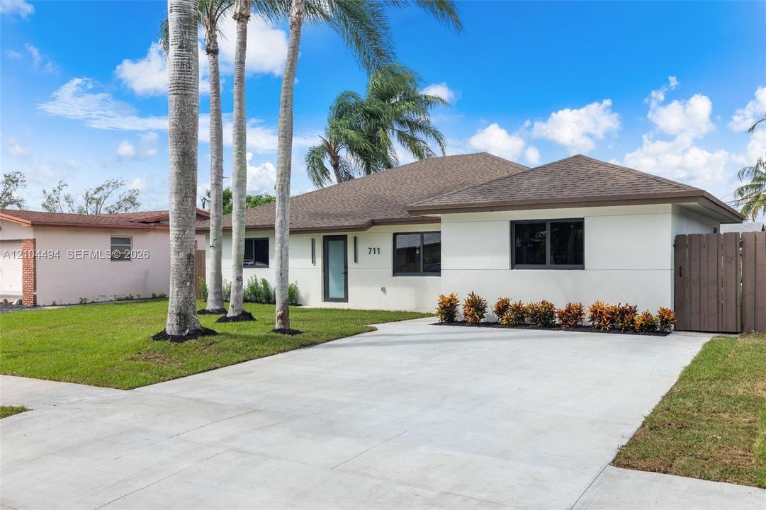 Single-story residence featuring a neutral stucco exterior, a concrete driveway, modern dark-framed windows, and a privacy fence