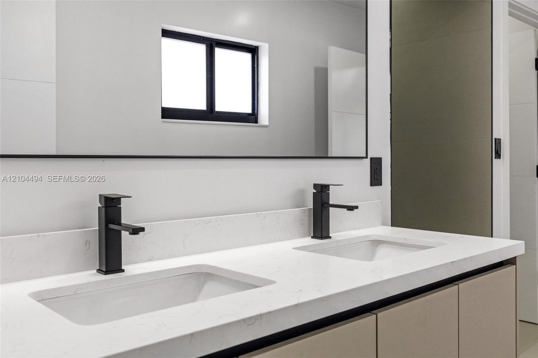 Dual-sink vanity featuring a light-toned countertop, undermount basins, matte black hardware, and an expansive wall-to-wall mirror