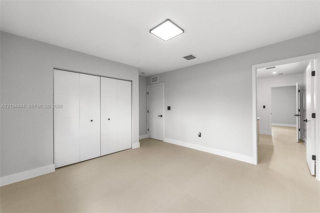 Neutral-toned room featuring large-format tile flooring, recessed square ceiling lighting, white flush-panel closet doors, and matte black door hardware