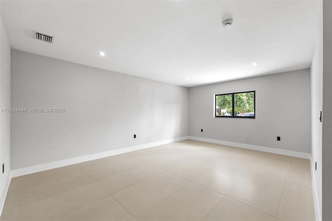 Interior space featuring neutral wall tones, large-format tile flooring, recessed ceiling lighting, and a single window with a black frame