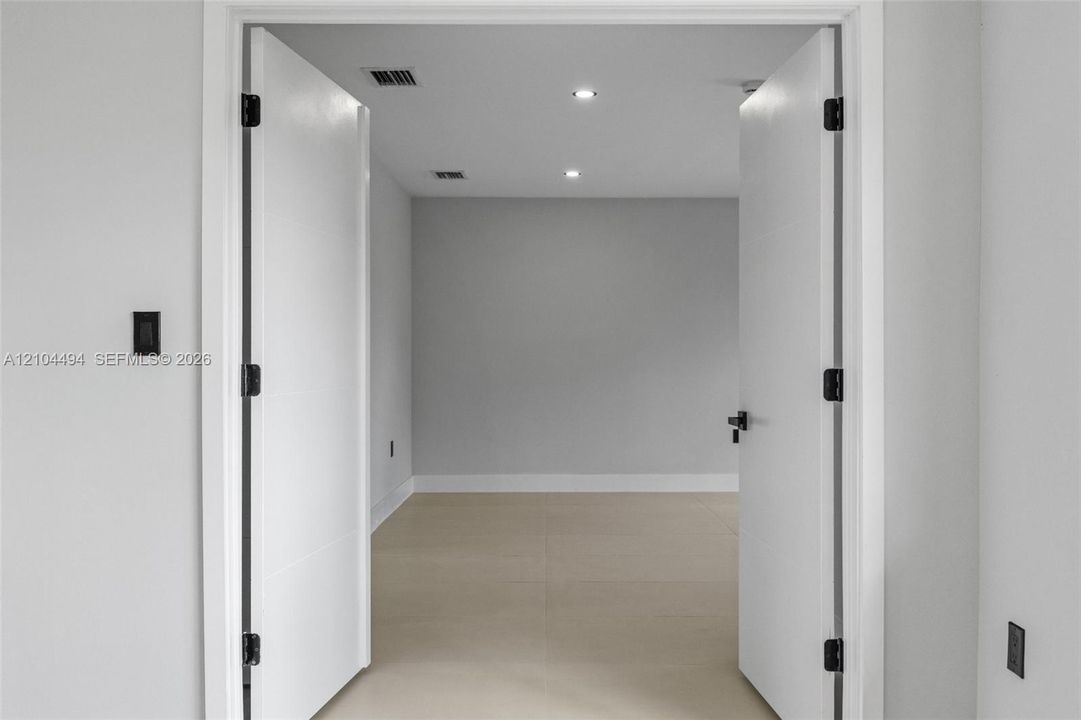 Double interior doors featuring matte black hardware, recessed ceiling lighting, and neutral large-format tile flooring