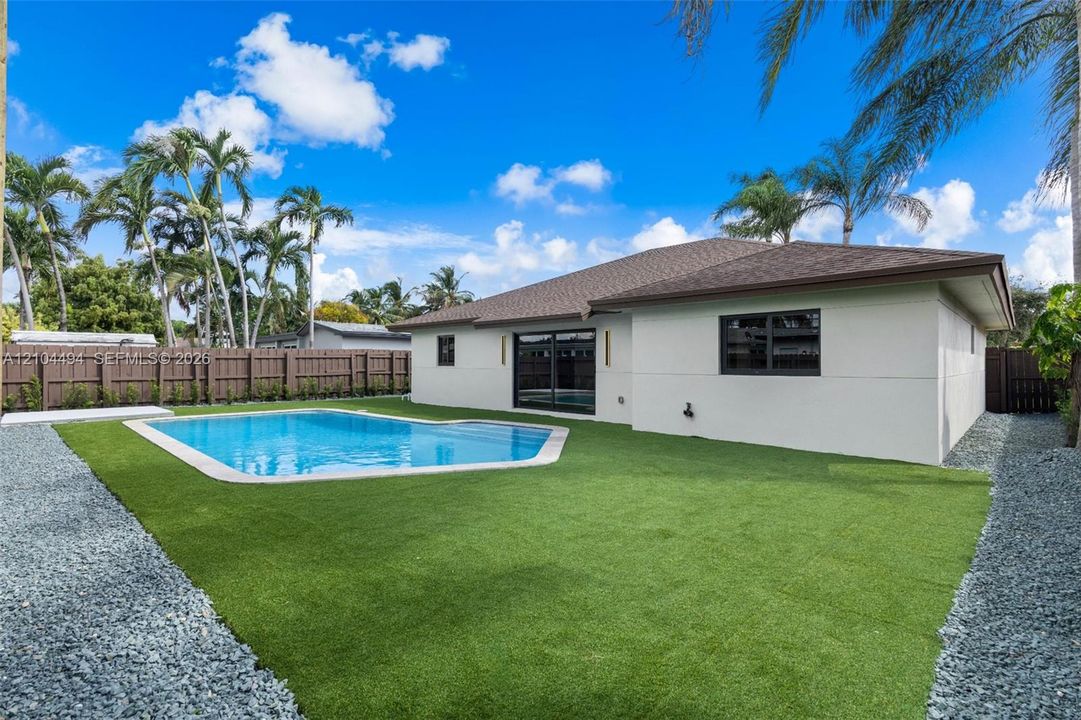 Backyard featuring an in-ground swimming pool, synthetic turf lawn, stone-surfaced side border, and wood-finish privacy fencing