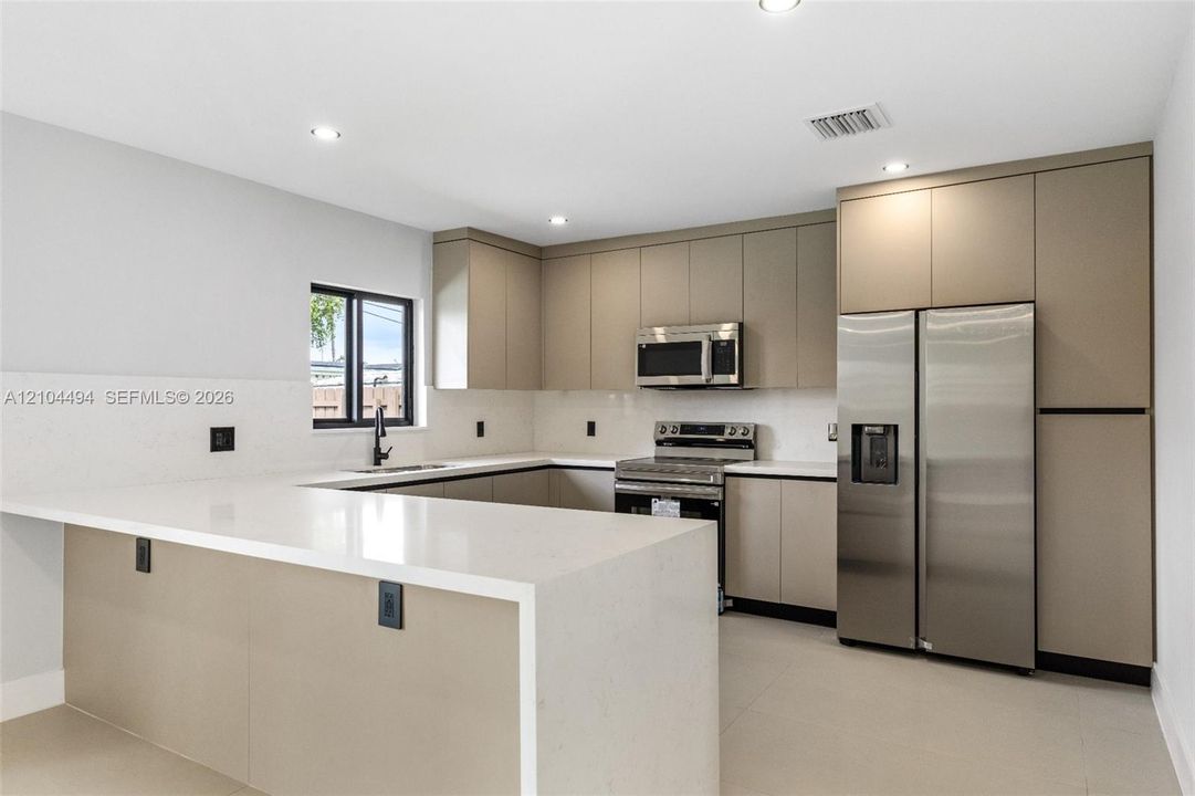 Kitchen featuring flat-panel cabinetry, quartz countertops with a waterfall edge, stainless steel appliances, and recessed lighting