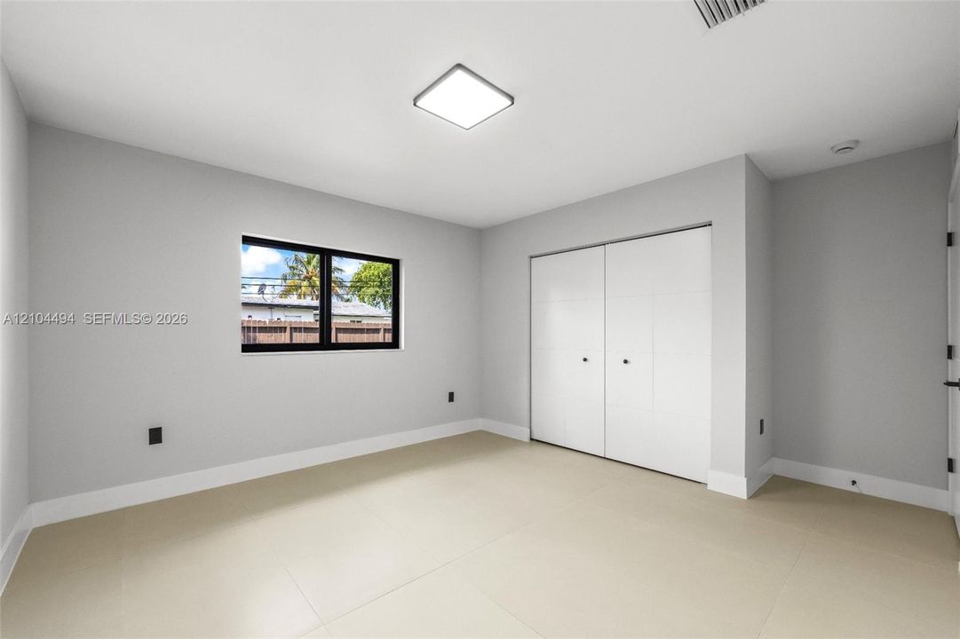 Neutral-toned room featuring large-format tile flooring, a square flush-mount LED fixture, a black-framed window, and a built-in closet with double doors