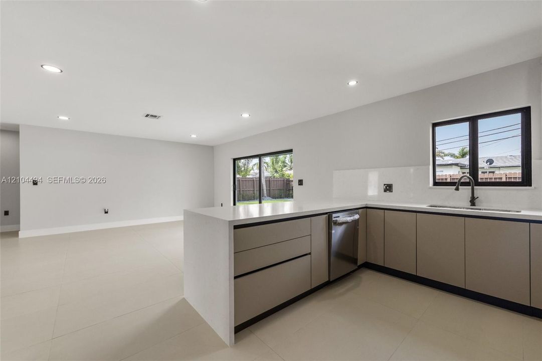 Kitchen featuring flat-panel cabinetry, light-toned stone-finish countertops, recessed ceiling lighting, large-format tile flooring, and matte black plumbing fixtures