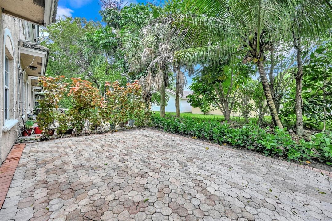 Outdoor patio featuring hexagonal concrete pavers, surrounded by mature palm trees and lush landscaping
