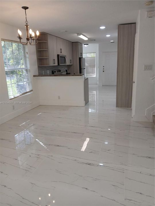 Kitchen featuring light wood-finish cabinetry, stainless steel appliances, dark countertops, and polished large-format tile flooring