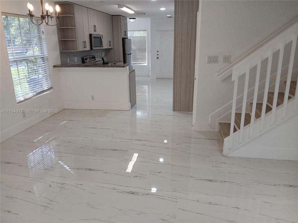 Kitchen featuring wood-finish cabinetry, stone-style countertops, stainless steel appliances, and large-format tile flooring