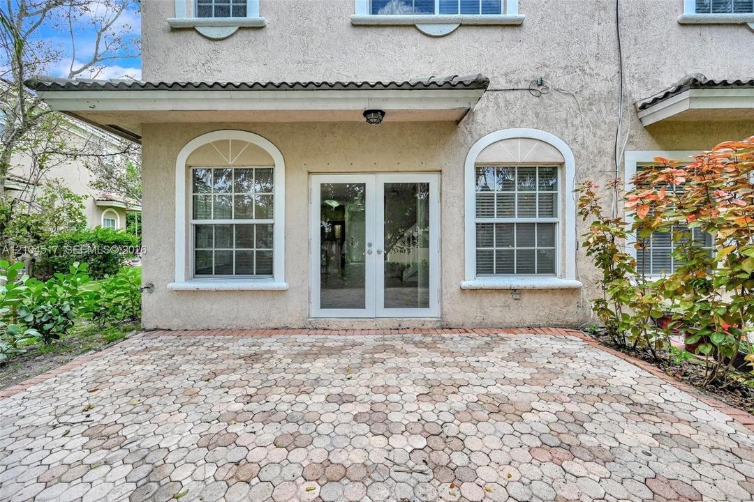 Stucco exterior patio featuring a decorative stone paver surface, glass-paneled double doors, and arched window frames