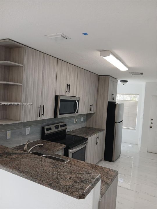 Kitchen featuring light-toned cabinetry, stainless steel appliances, dark stone-finish countertops, and white tile flooring with gray veining