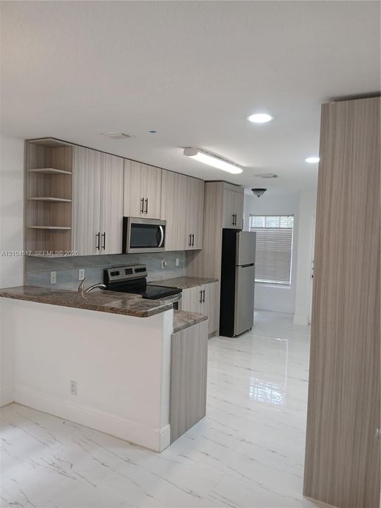 Kitchen featuring light wood-finish cabinetry, stainless steel appliances, stone-look countertops, and high-gloss tile flooring with recessed lighting