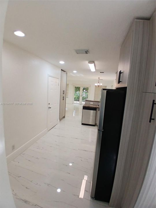 Kitchen featuring light wood-finish cabinetry, stainless steel appliances, stone-finish countertops, tile backsplash, and polished stone-finish flooring