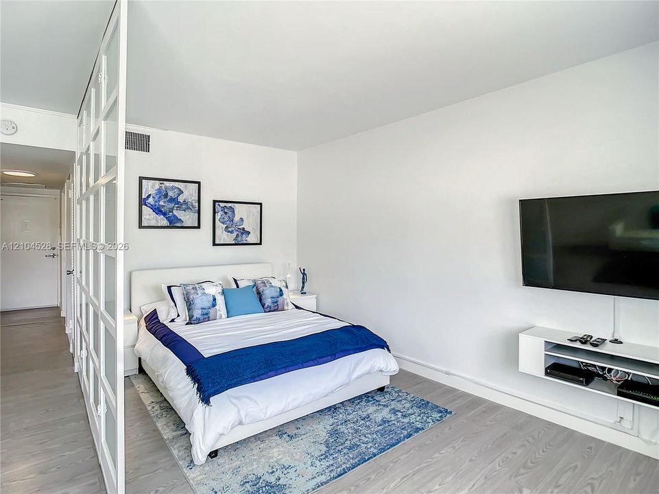 Wood-finish flooring, white floor-to-ceiling glass-paned room partition, and wall-mounted white media console