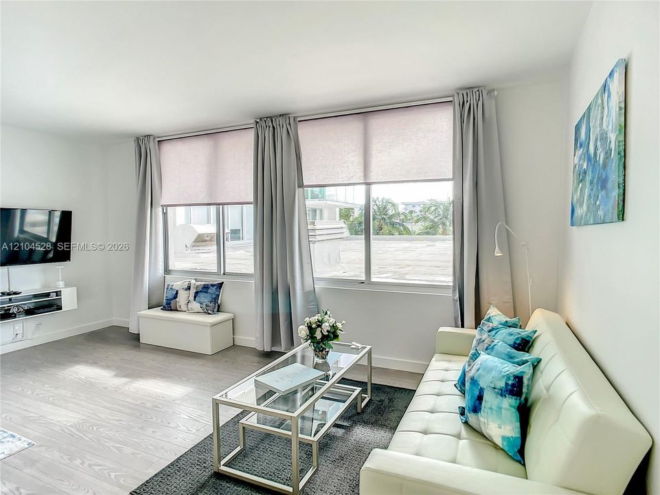 Neutral wall-to-wall wood-finish flooring, expansive windows with integrated roller shades, and a wall-mounted floating media console