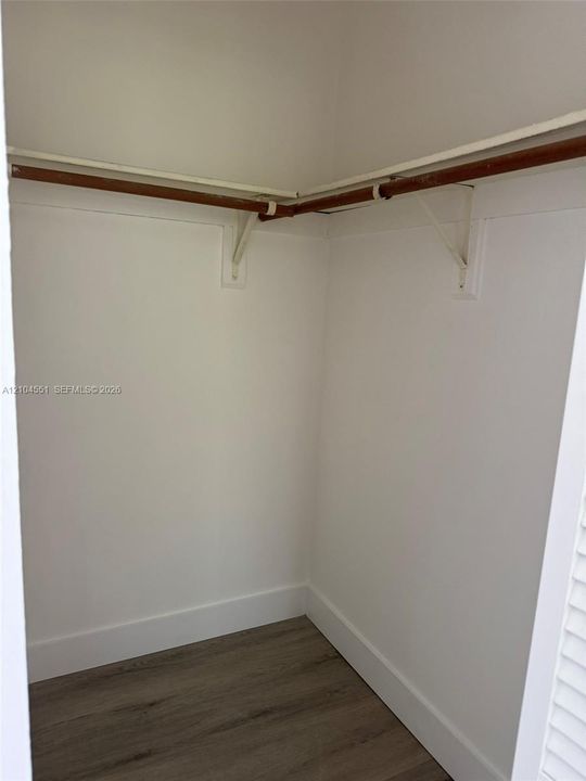 Storage area featuring wood-finish flooring, white walls, and built-in shelving with hanging rods