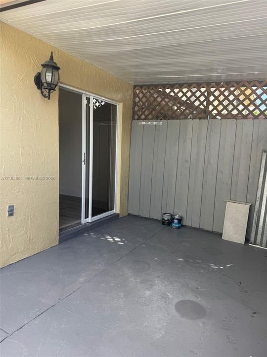 Covered concrete patio featuring white-framed sliding glass doors, exterior wall-mounted lantern lighting, and wood-paneled privacy fencing with lattice accents