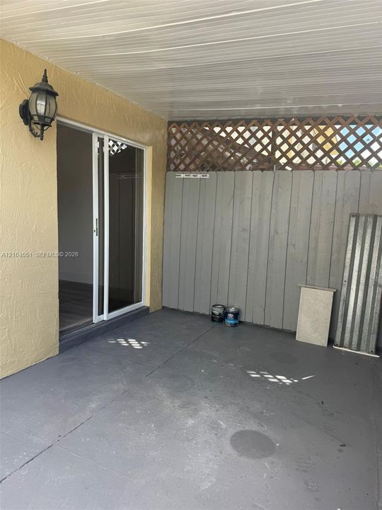 Covered patio featuring concrete flooring, sliding glass door access, exterior wall-mounted lighting, and a vertical wood privacy screen with lattice detailing