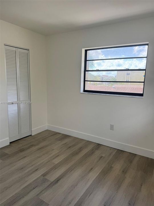 Wood-finish flooring, white louvered closet doors, and a horizontal jalousie window