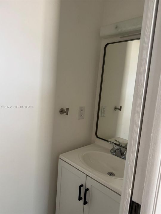 White cabinetry with matte black hardware, integrated vanity sink, brushed metal faucet, rectangular mirror with dark metal frame, and wall-mounted metal hardware