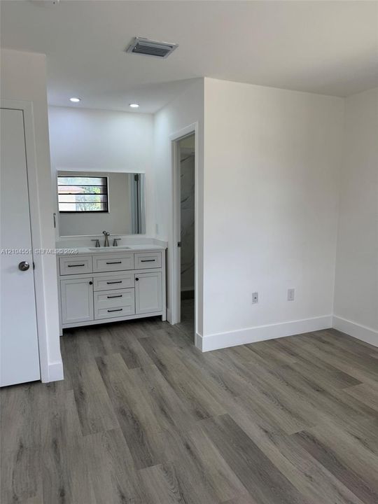 White vanity cabinet with dark hardware, rectangular undermount sink, recessed lighting, and wood-finish flooring