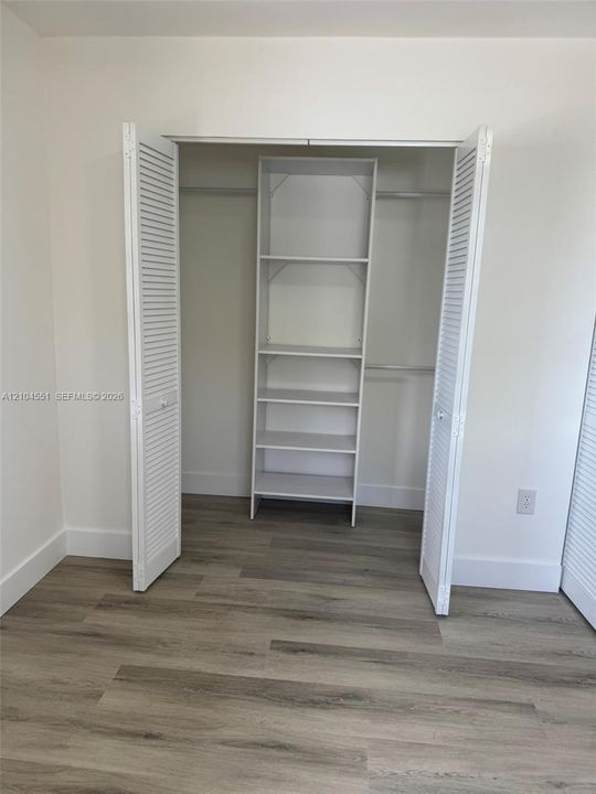 Closet featuring white louvered bifold doors, built-in shelving, and wood-finish flooring