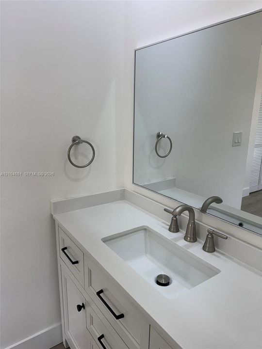 White vanity featuring an undermount rectangular sink, light-toned solid surface countertop, brushed nickel widespread faucet, and matte black hardware paired with a wall-mounted mirror