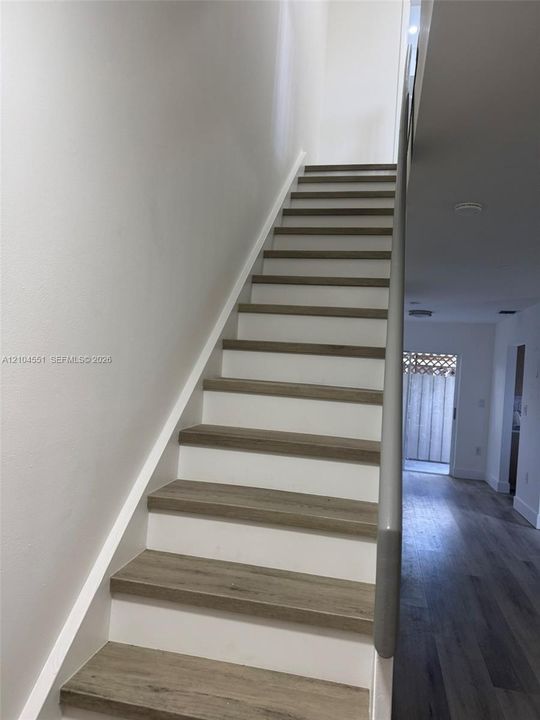 Staircase featuring wood-finish treads, white risers, and a neutral-toned handrail