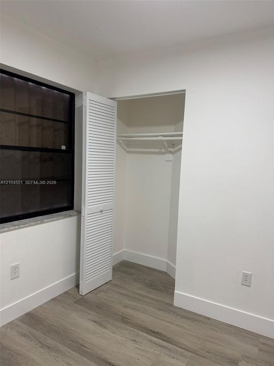 Multi-panel black-frame window with stone sill, wood-finish flooring, and closet featuring white louvered doors and a built-in rod