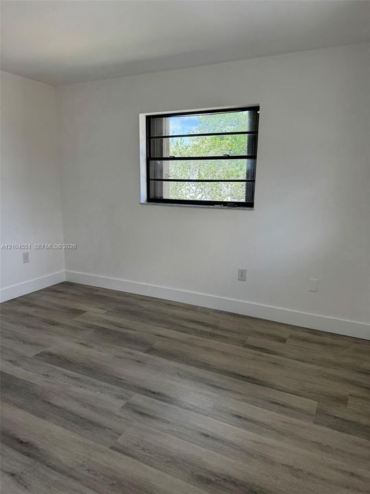 Neutral interior featuring wood-finish flooring, white walls, and a horizontal window with dark-toned framing